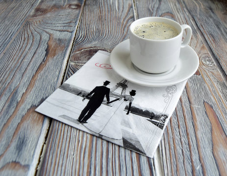 Чашка с кофе и салфетка с символом Парижа   лежат на деревянном столе