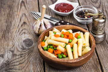 Pasta with carrots and green peas in wooden bowl