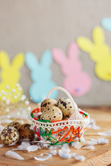Easter composition of Easter quail eggs in the basket and with bunny garland on wooden background