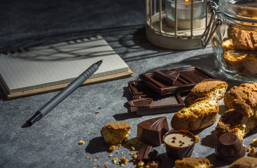 Tasty and healthy almond cookies, rich in vitamins, minerals in a glass jar, chocolates and notebook on a dark background. Low key.