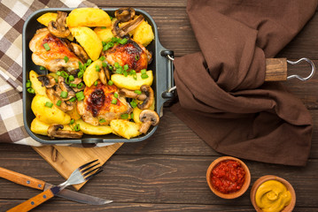 Dinner with baked chicken legs with olives spiced with aromatic herbs and potatoes with mushrooms on a rustic background. Top view, copy space.