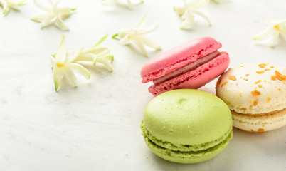 Varicolored macaroons and flowers on a white background in light key. Copy space.