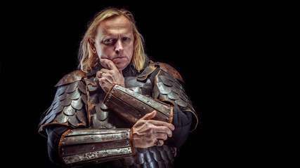Powerful blond knight is standing deep in thoughts. Dark background