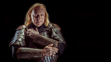 Powerful blond knight is standing deep in thoughts. Dark background