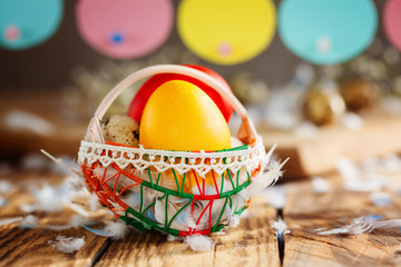 Easter composition of Easter colorful eggs in the basket and with bunny garland on wooden background.