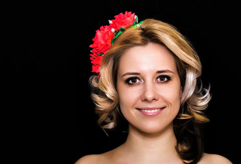 Woman with blonde laying and rimmed with red flowers on a dark background smiling. Close-up. Space for text
