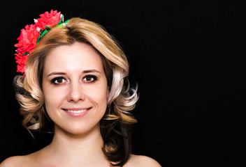 Woman with blonde laying and rimmed with red flowers on a dark background smiling. Close-up. Space for text