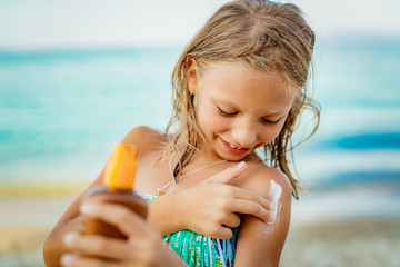Little Girl applying sunscreen lotion on the beach