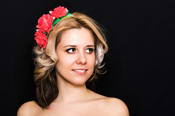 Naklejka premium Kobieta z blond r. I oprawione w czerwone kwiaty na ciemnym tle uśmiechnięty. Zbliżenie. Miejsce na tekst