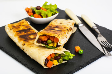 Roll from lavash with vegetables on black stone