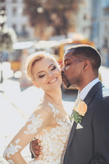 Happy african American groom and cute bride walking on street