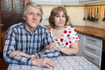 Caucasian elderly couple sitting at the kitchen dinner table and looking at camera