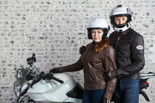 Young man and woman in a motorcycling outfit stand together with the motorbike in the garage