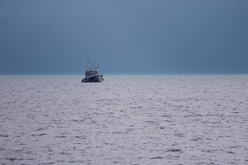 Small fishing boat returning to the shore under dark stormy sky, Gulf of Thailand
