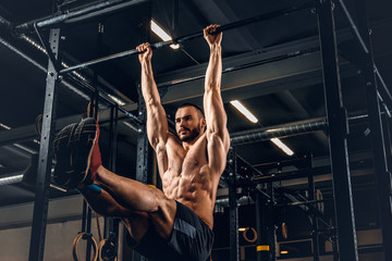 A man doing ABS workouts on pull up bar in a gym club.