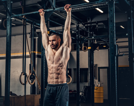 A man doing ABS workouts on pull up bar in a gym club.