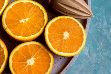 Ripe colorful oranges cut in half on stone platter with wood reamer by window, top view close up