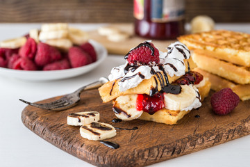 Belgian waffles with raspberries, bananas and double cream on rustic table.