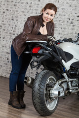 Full-length portrait of woman a motorcyclist with vintage street style standing near a modern motorbike