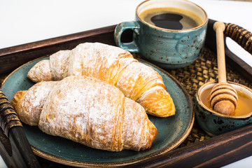 Croissant, honey and espresso in blue vintage bowl on wooden tra