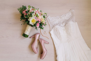 Bridal morning details. Wedding rings, beautiful bouquet of yellow and pink flowers, white wedding dress and leather shoes.