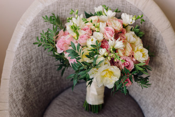 Bridal morning details. Wedding bouquet of yellow, beige and pink flowers with greenery on a chair.