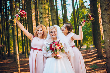 Bride with bridesmaids with wedding bouquet at hand on sunny forest.