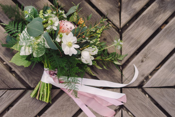 Botanic bridal chic. Wedding bouquet with silk ribbons and protea flowers on wooden background in sunlight.