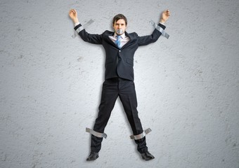Businessman in suit is taped to the wall with adhesive tape.