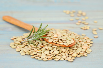 Pile of lentils with rosemary and wooden spoon on blue background