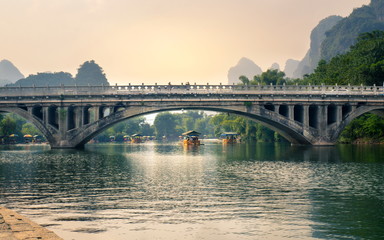 YANGSHUO, CHINA - SEPTEMBER 23, 2016: Boats with tourists floating on Li River, below a stone bridge at sunset