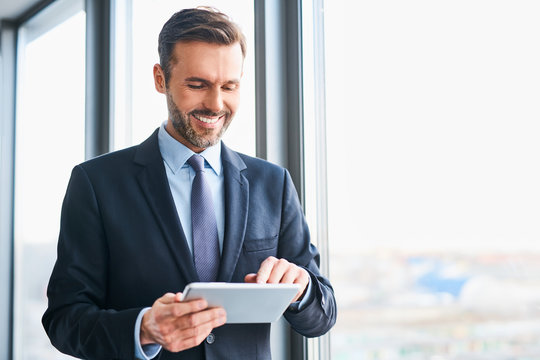 Happy businessman using digital tablet standing in office