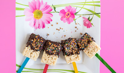 horizontal image of rice krispie bars dipped in chocolate and sprinkled with sprinkles lying on a white plate with pink flowers.