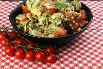 Bowl of tricolor tortellini pasta salad with tomatoes and onions on dark wood table background