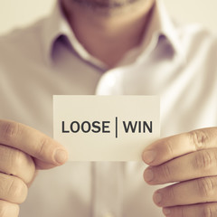 Businessman holding LOOSE WIN message card
