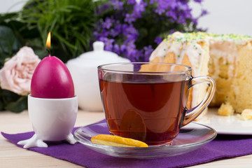 Cup of tea with lemon slice with a piece of cake in icing with sprinkles on a purple tablecloth and...