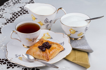 Cup of tea and cake on porcelain tableware for the white embroidered tablecloth and paper napkins