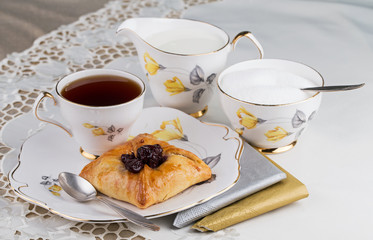 Cup of tea and cake on porcelain tableware for the white embroidered tablecloth and paper napkins
