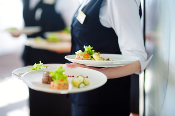 Waiter carrying plates with meat dish on some festive event - obrazy, fototapety, plakaty