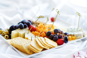 Different kinds of wine snacks: cheeses, crackers, fruits and olives on white table