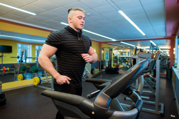 Attractive young muscular man while running on a treadmill in gym