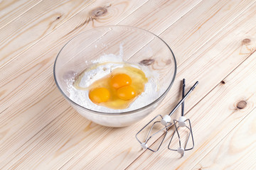 Ingredients for home-grandmother lemon in a glass bowl on a table with light wood; eggs broken into a bowl before mixing