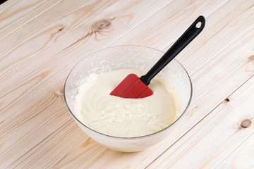 mass homemade cake in a glass bowl on a table with light wood; cake prepared to pour into molds and baking

