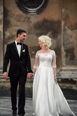 Fototapeta premium Stylish beautiful happy newlywed couple walking together holding each other hands