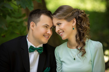 Wedding couple, elegant groom with green bow and beautiful bride in mint dress looking at each other in green park