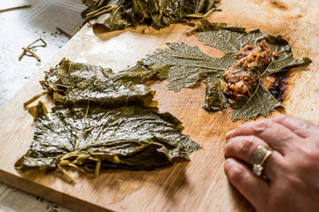 Woman is wrapping grape leaves for turkish dolma with minced meat.