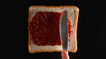 TOP VIEW: Human hand spreads a raspberry jam on a bread © Cliplab