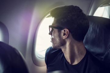 Side view of handsome young man against plane window sitting and looking out