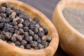 Black peppercorns and powder in a bamboo bowl