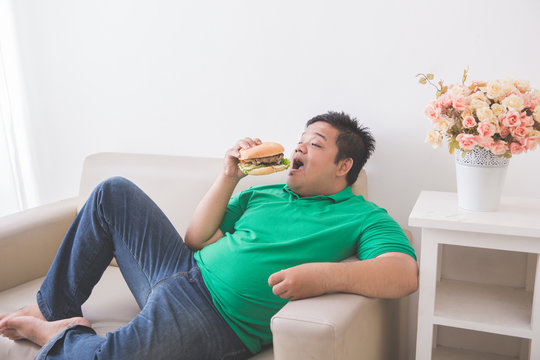 lazy overweight man eating hamburger while laying on a couch